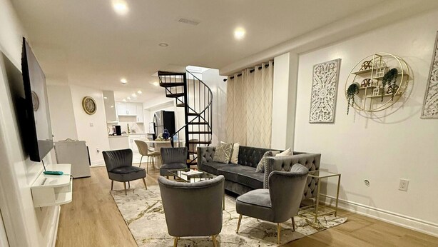 A modern living room with a sofa, armchairs, and a coffee table. There is a spiral staircase leading to an upper level. - Guest Suite in the Heart of Mississauga (Mississauga)