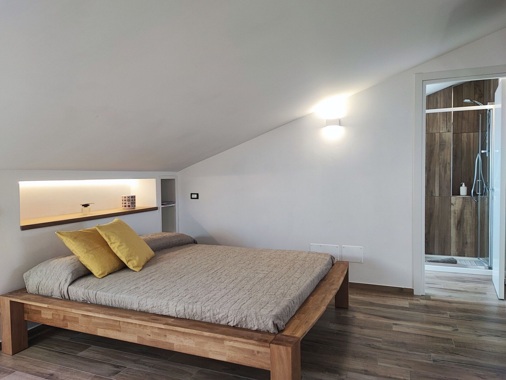 A bedroom with a bed, a bedside table, a wall-mounted shelf, and a shower area.
