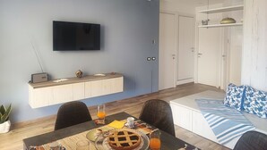 A modern living room with a flat-screen TV, a dining table with breakfast items, a sofa with patterned cushions, and a white wardrobe. - Italian Experience- Casa Nadia (Numana)