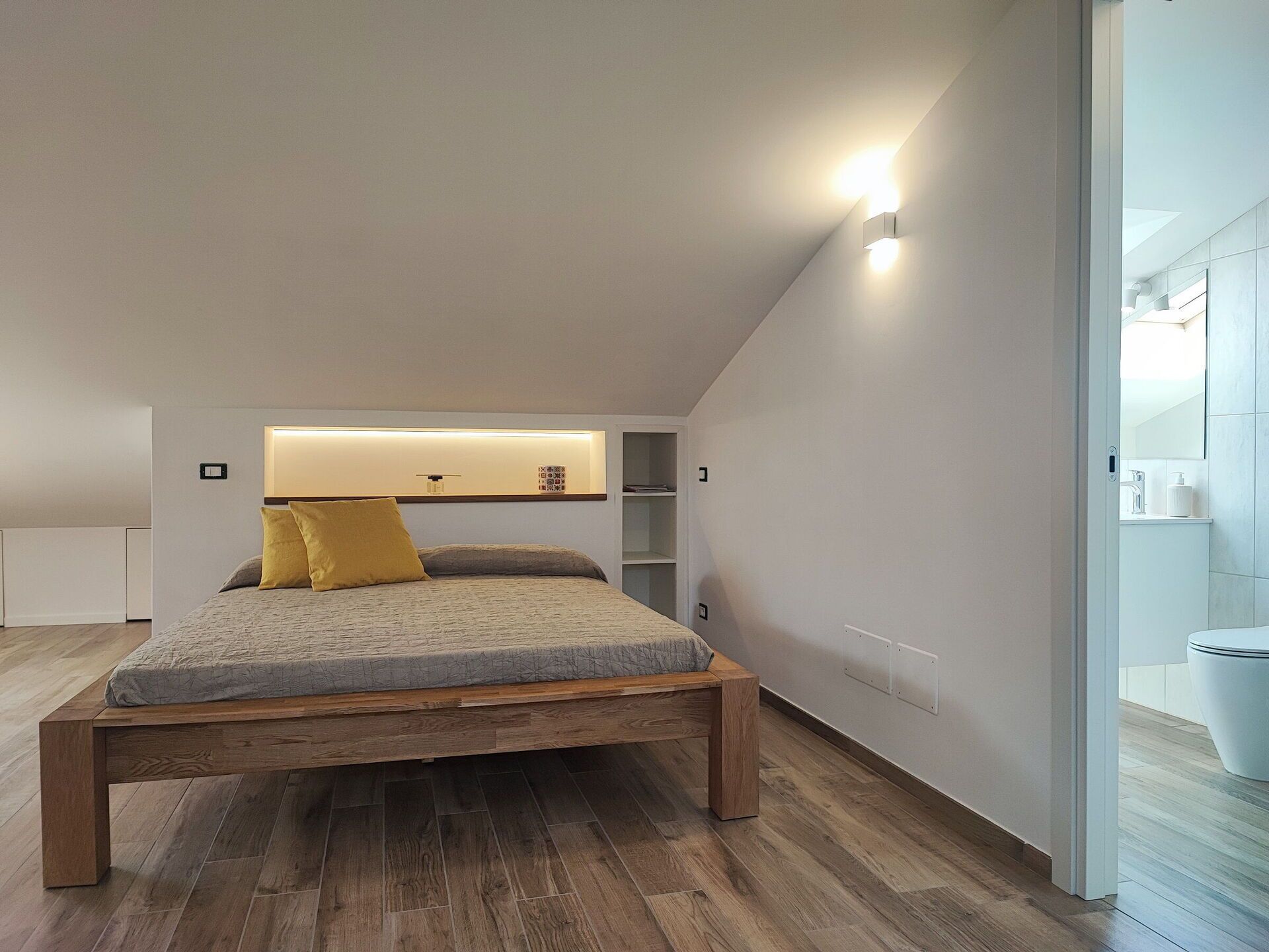 A modern bedroom with a wooden bed, a built-in shelf, and a white wall.