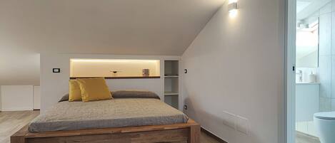 A modern bedroom with a wooden bed, a built-in shelf, and a white wall.