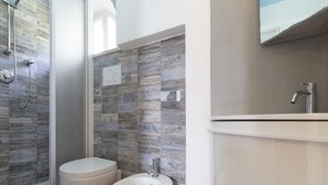 Un bany amb dutxa, vàter, bidet i un mirall sobre el lavabo.