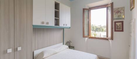 A bedroom with a bed, a wardrobe, a window with a view, and a door.
