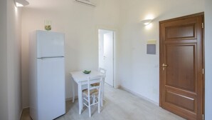 Una cuina compacta amb un frigorífic blanc, una taula petita amb una cadira i una porta de fusta.