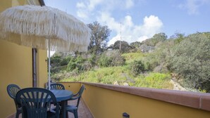 Un pati amb taula i cadires, un parasol de palla i vista a un paisatge amb muntanyes.