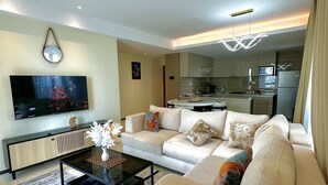 Ein modernes Wohnzimmer mit einer Couch, einem Couchtisch und einem Fernseher. Im Hintergrund ist eine Küche zu sehen.