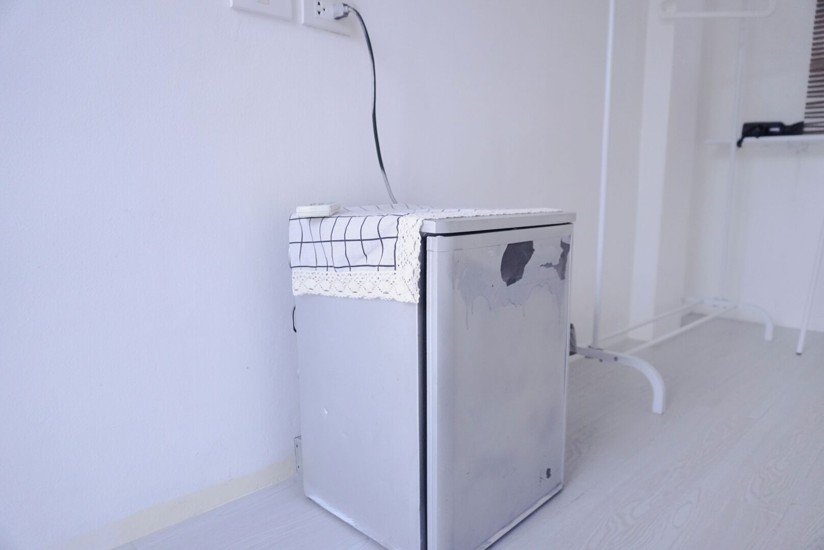 A compact, white appliance, possibly a refrigerator, in a room with white walls and a wooden floor.