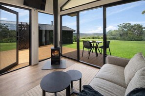 A modern living room with a wood-burning stove, large sliding glass doors, a sofa, and a small table. - New Luxe Villa - Coastal Views - 30 min to Noosa (Ninderry)