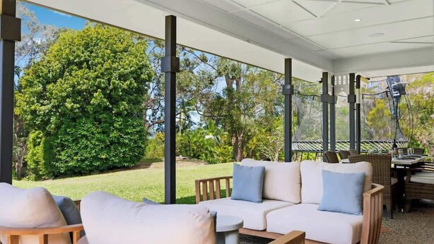 A covered outdoor seating area with a sofa and chairs, a table, and a view of a lush garden. - Hinterland Escape - Coastal Views, Pool & Fire Pit (Ninderry)
