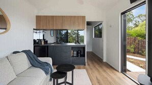 A modern kitchen with a wooden upper cabinet, a built-in sink, and a coffee machine. There is a small black table and a grey sofa with a blue throw blanket. - Luxe Villa - Ocean Views, 15km to Coolum Beach (Ninderry)
