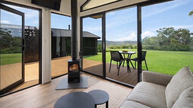 A modern living room with a wood-burning stove, large sliding glass doors, and a view of a green landscape. - Luxe Villa - Ocean Views, 15km to Coolum Beach (Ninderry)