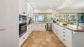 Una cocina moderna con armarios blancos, electrodomésticos de acero inoxidable y un amplio ventanal con vistas al exterior.