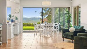 Una cocina moderna con armarios blancos, un comedor con sillas blancas y un amplio ventanal corredero que da a una vista panorámica del exterior.