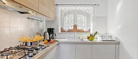 A kitchen with a gas stove, a sink, and a window with a curtain.