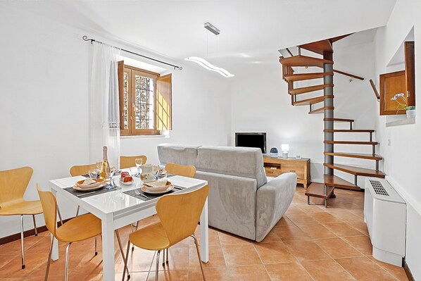 A modern living space with a dining area, sofa, TV, and a spiral staircase. - Toscolano Olive House (Toscolano Maderno)