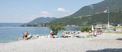 A pebbled beach with people, a boat, and a mountain in the background.