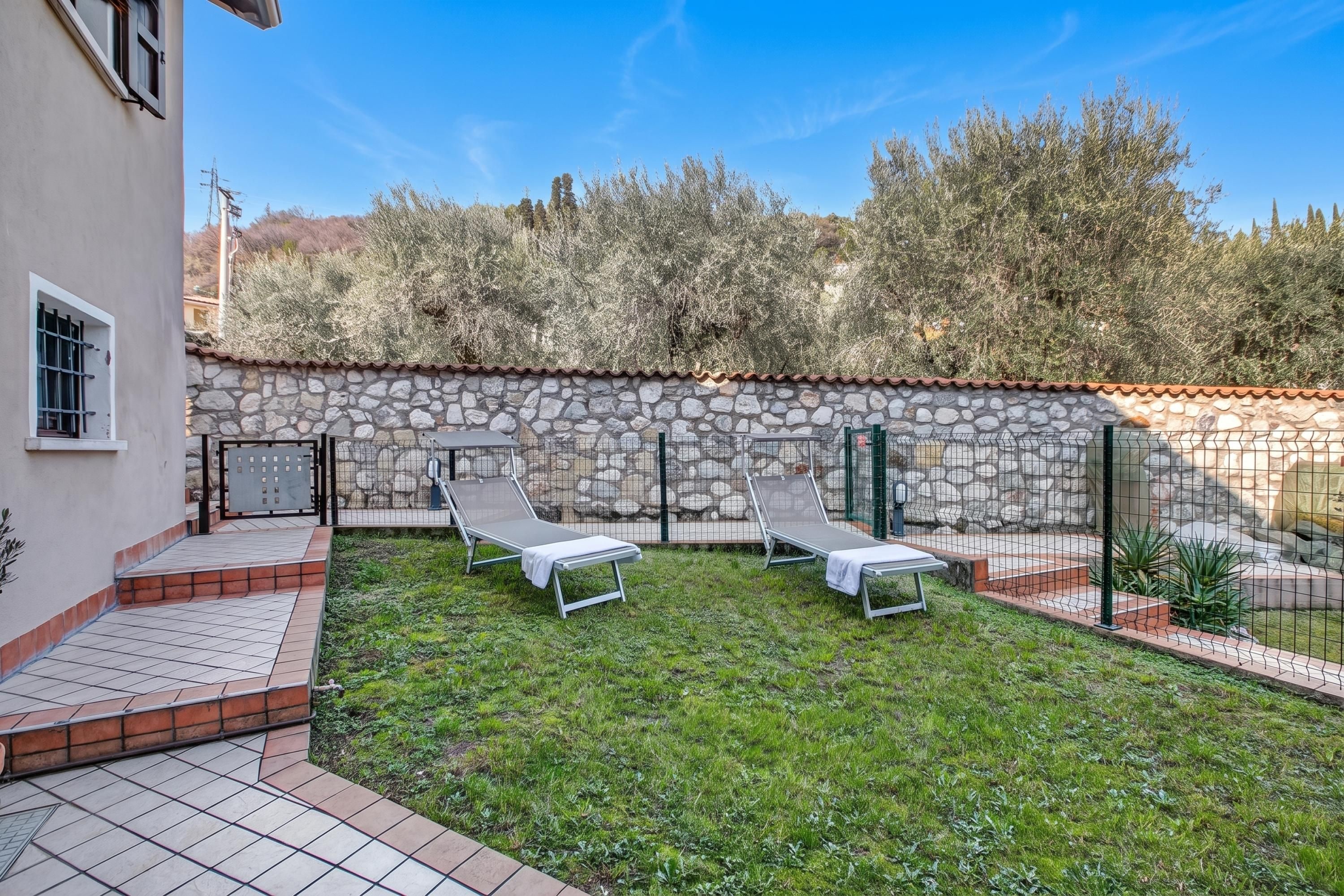 Une cour avec deux fauteuils de jardin, un mur en pierre et une terrasse carrelée.