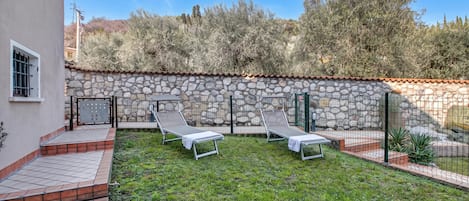 Une cour avec deux fauteuils de jardin, un mur en pierre et une terrasse carrelée.