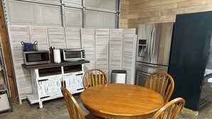 A dining area with a round wooden table and four chairs, a white cabinet with a microwave and toaster, and a stainless steel refrigerator. - Escape to the peaceful, Cottage 3:12 at Suttle Ridge in Arkadelphia, AR (Arkadelphia)