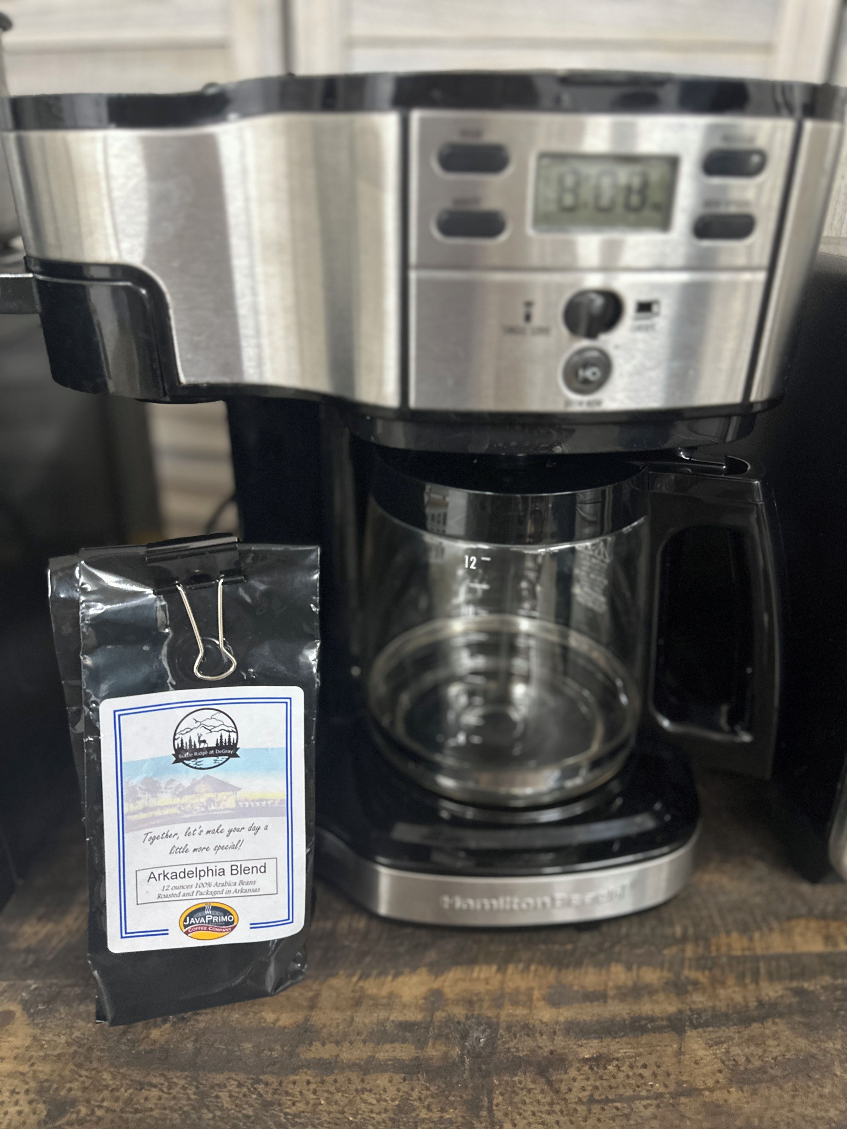 Kahvinkeitin, jossa on digitaalinen näyttö, lasinen kahvikannu ja kahvipaketti, jonka etiketissä lukee ”Arkadelphia Blend”.