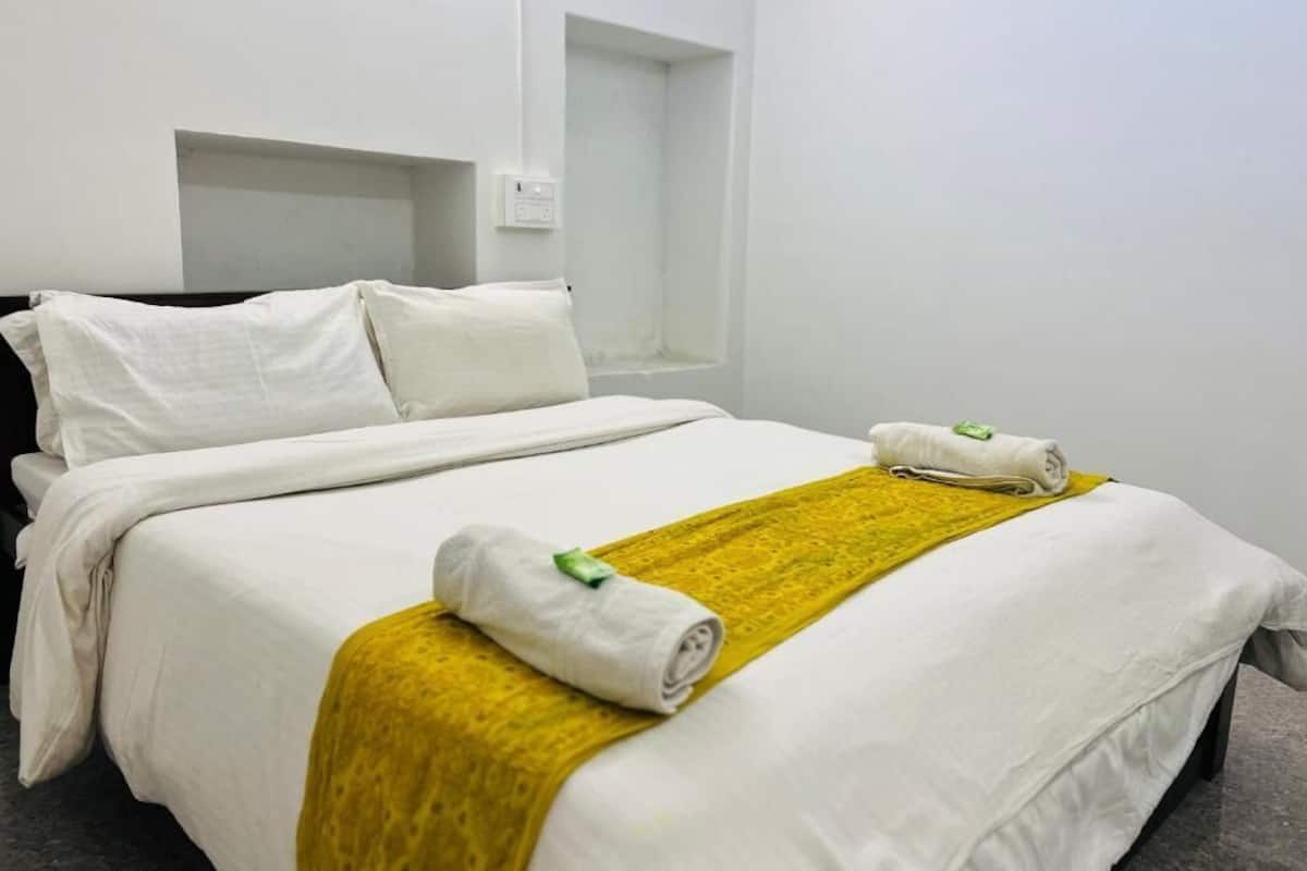 Een hotelkamer met een net opgemaakt bed, een gele plaid en een handdoek op het bed.