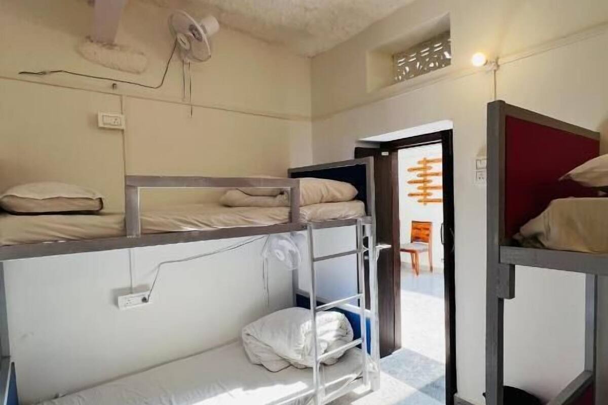 Een slaapzaal met stapelbedden, een plafondventilator en een deur die naar een andere kamer leidt.