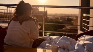 Iemand zit aan een tafel op een balkon met uitzicht op een zonsondergang en stadsbeeld.