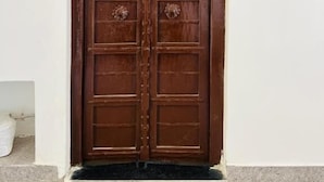 Een houten dubbele deur met een metalen handgreep en decoratieve details, ingebouwd in een witte muur met een stenen basis.