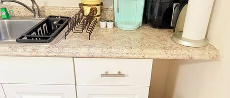 A kitchen with a sink, a coffee maker, a paper towel dispenser, and a trash can.