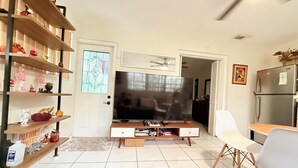 Een woonkamer met een televisie, houten planken, een witte stoel en een keukenhoek.