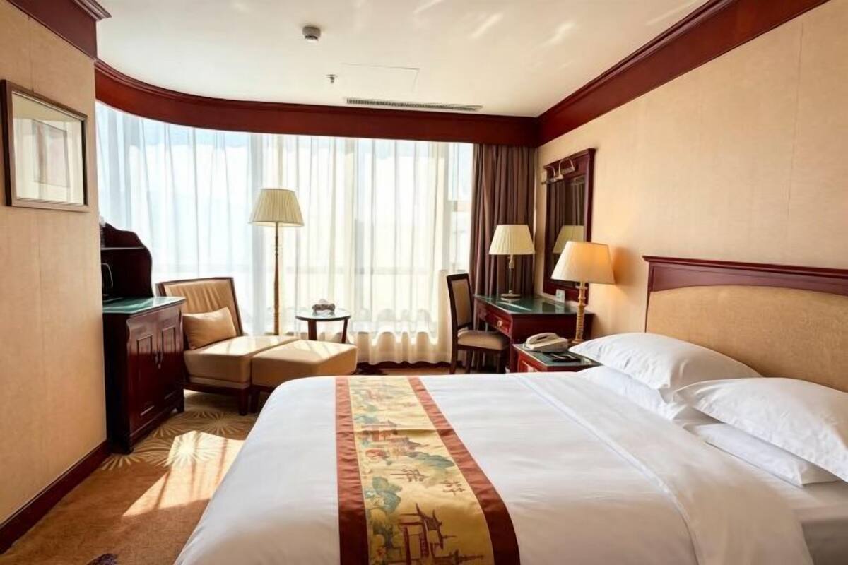 A hotel room with a large bed, a desk, a chair, a lamp, and a window with curtains.