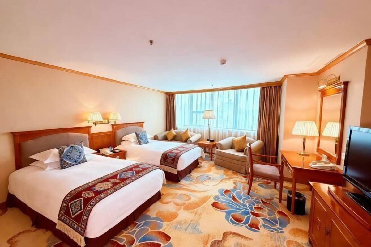 A hotel room with two beds, a sofa, a TV, and a desk.