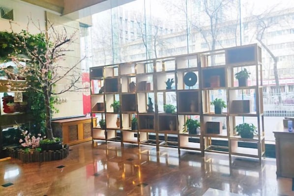 A modern interior with a wooden floor, a glass partition with shelves, and a large window with a view of trees and buildings.