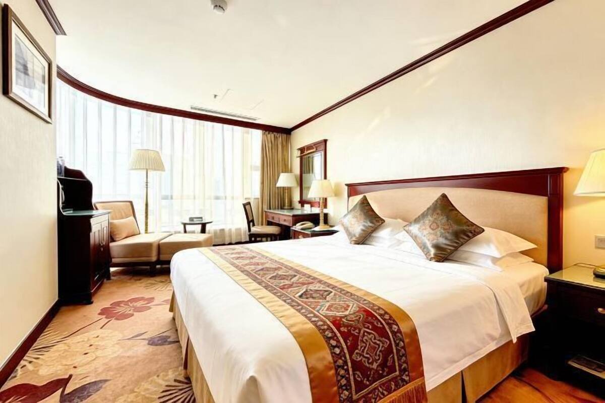 A hotel room with a large bed, a desk, a chair, a lamp, and a window with curtains.