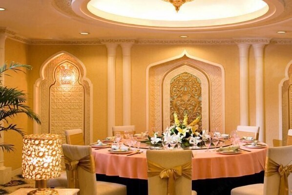 A dining area with a round table set for four, adorned with a pink tablecloth and gold chair sashes.