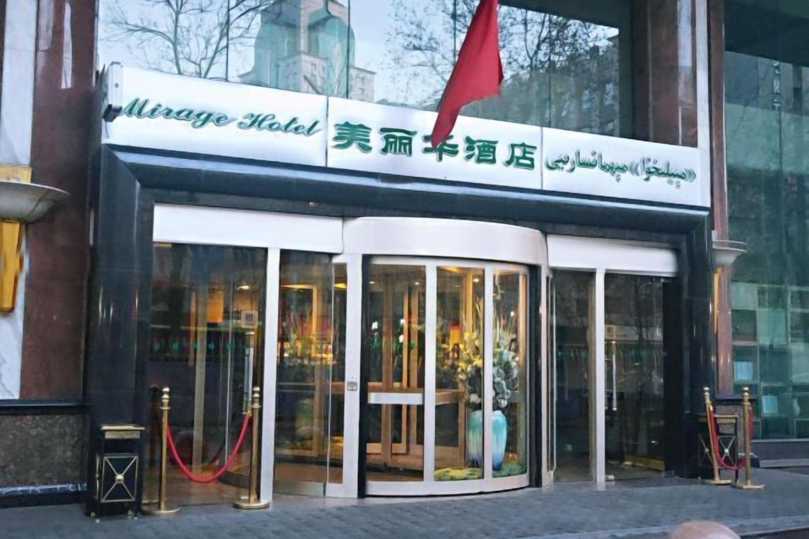 A hotel entrance with a glass facade, a red flag, and a sign in multiple languages.