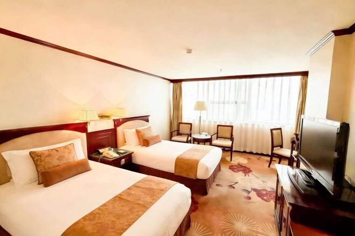 A hotel room with two beds, a TV, a desk, and a chair.