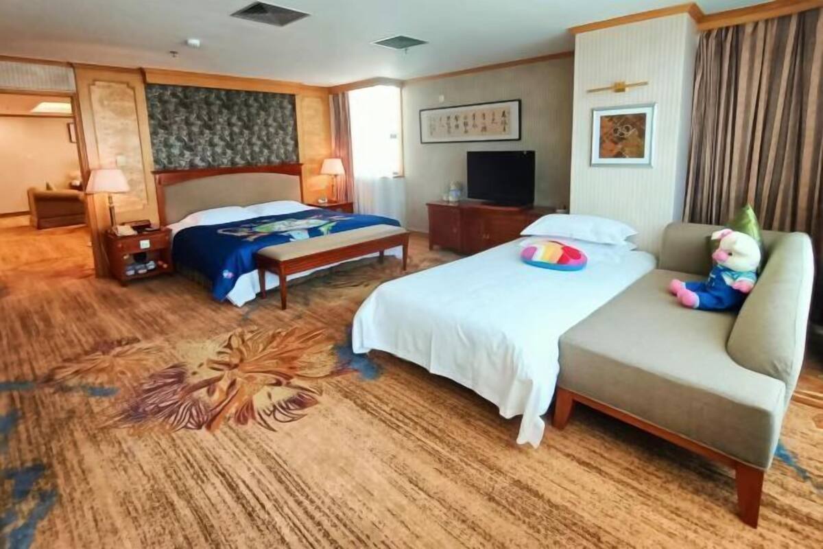 A hotel room with a large bed, a sofa, a television, and a plush toy.