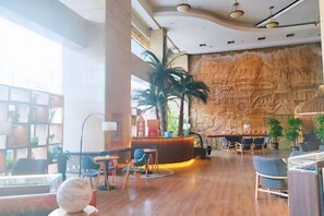 A lobby with a reception desk, seating area, and a large wall mural. - Miramar Urumqi (CCMALL Hongshan Park Times Square Branch) (Urumqi)