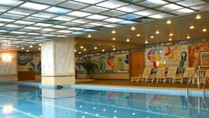 Una piscina interior con techo azulejado, murales coloridos en las paredes y sillas de descanso.