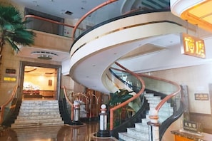A modern hotel lobby with a curved staircase, marble flooring, and a reception desk.