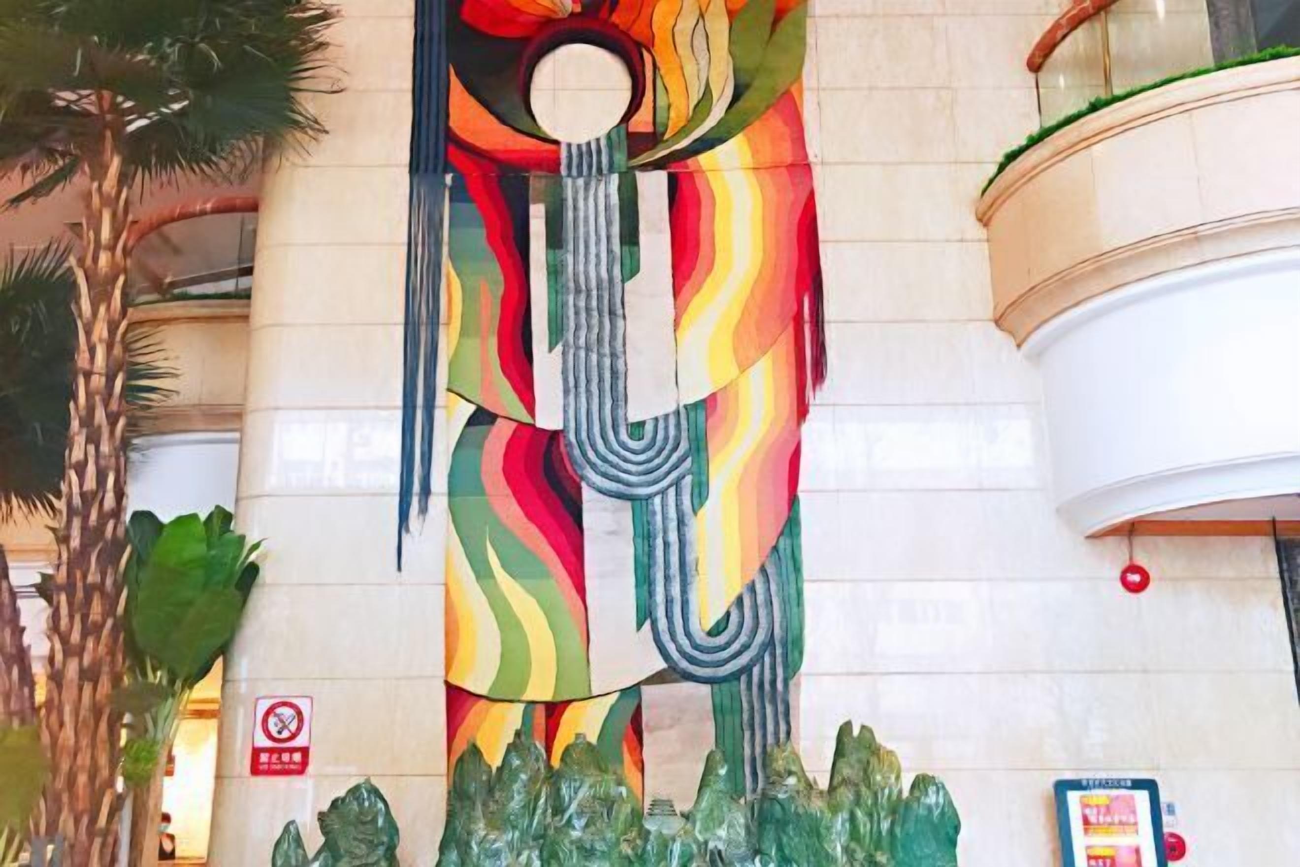 A colorful abstract sculpture in a lobby with a palm tree and a no-smoking sign.