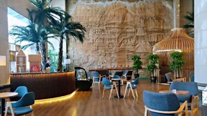 Un moderno vestíbulo con suelo de madera, asientos azules, un mostrador de recepción y una amplia pared de piedra con relieves.