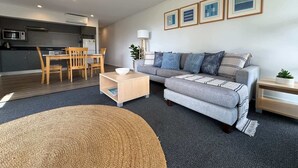 Ein modernes Wohnzimmer mit einem grauen Sofa, einem Holzesstisch und einer Küche im Hintergrund.