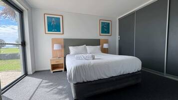 Une chambre d’hôtel moderne avec un grand lit, deux tables de chevet avec des lampes, une armoire et deux œuvres d’art encadrées accrochées aux murs.