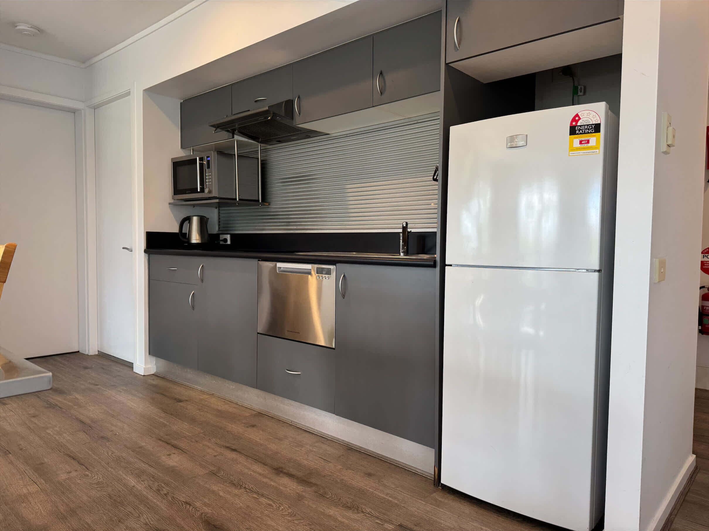 A modern kitchen with stainless steel appliances, grey cabinetry, and a white refrigerator.