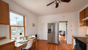 Una cocina moderna con suelo de madera, un refrigerador de acero inoxidable, una mesa de comedor con sillas y un ventilador de techo.
