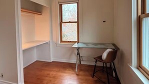 Una habitación con suelo de madera, una ventana, un escritorio y una silla.