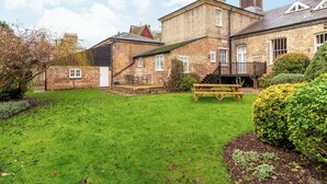 A traditional brick house with a spacious lawn, a wooden bench, and a staircase leading to a deck. - Stearn Cottage-17917 (Bury St. Edmunds)