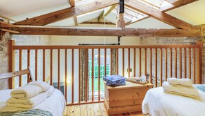 A room with wooden beams, a bed, a wooden chest of drawers, and a view through a window. - Stearn Cottage-17917 (Bury St. Edmunds)